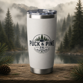 White Puck & Pine Co. insulated tumbler featuring a hockey and pine tree logo with a misty forest and mountain backdrop.